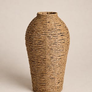 May include: A tall, cylindrical vase crafted from woven light brown natural fibers. The vessel features a narrow, circular opening at the top, a slightly wider midsection, and a flat base, showcasing a consistent horizontal weave pattern throughout.