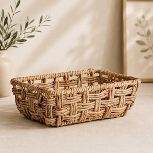 May include: A rectangular storage basket crafted from natural light brown woven seagrass. The basket features an open, grid-like lattice pattern with thick, sturdy reeds interlaced to form the base and walls, creating a structured, hollow container.