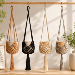 May include: Four macrame plant hangers suspended from a wooden rod, each featuring a knotted diamond pattern and a long tassel. The hangers come in four distinct colors: mustard yellow, black, cream, and light gray, each holding a solid ceramic pot.
