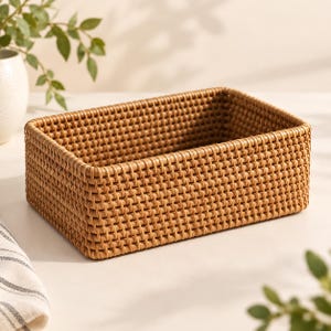 May include: A rectangular storage basket crafted from light brown woven material. The basket features a consistent, tight grid pattern throughout its walls and base, creating a structured, open-top container with rounded corners and a uniform finish.