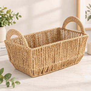 May include: A rectangular storage basket crafted from light tan woven material. The basket features an open-top design with vertical woven walls and two arched handles on the shorter sides, providing a structured and functional storage solution.