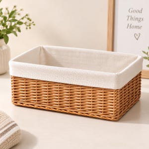 May include: A rectangular storage basket constructed from woven light brown wicker material. The interior of the basket is lined with a smooth, off-white fabric that folds over the top rim, creating a clean and structured appearance for organization.