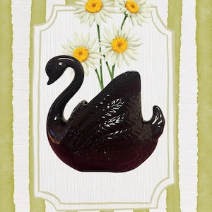 May include: A glossy black ceramic swan-shaped planter or vase holding three white daisies with yellow centers. The swan features molded feather details on its wings and is centered against a background of vertical olive green and white stripes.