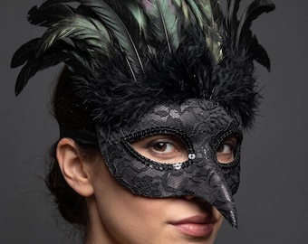 May include: A black masquerade mask featuring a pointed beak-like nose, intricate lace detailing, and a border of black sequins around the eye openings. The top of the mask is adorned with a dense arrangement of iridescent black and green feathers.