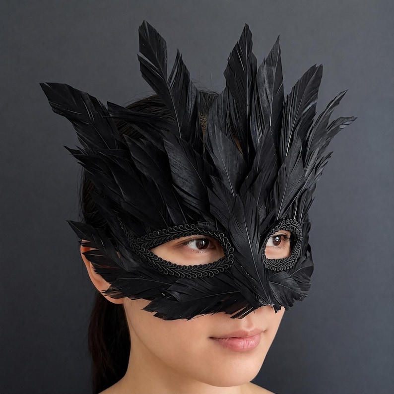 May include: A black masquerade mask adorned with numerous upright black feathers. The eye openings are framed with a decorative braided trim, and the feathers extend outwards from the centre to create a pointed, textured, and layered appearance.