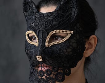 May include: A black lace cat mask featuring pointed ears and intricate floral embroidery patterns. The eye openings and the nose area are embellished with rows of small, sparkling gold-toned rhinestones, creating a defined feline facial structure.