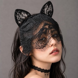 May include: A black lace headpiece featuring two upright cat ear shapes and a scalloped veil that partially covers the eyes. The accessory is crafted from intricate floral lace patterns and is paired with a matching black lace choker necklace.