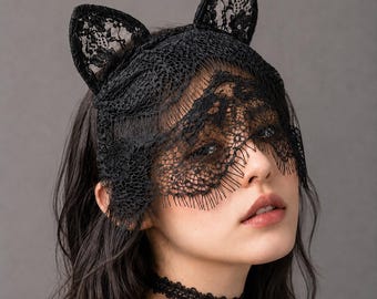 May include: A black lace headpiece featuring two upright cat ear shapes and a scalloped veil that partially covers the eyes. The accessory is crafted from intricate floral lace patterns and is paired with a matching black lace choker necklace.