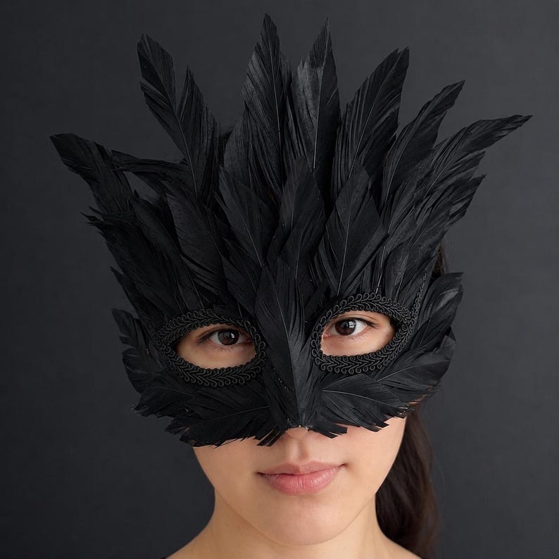 May include: A black mask covered in layered feathers that extend upwards and outwards. The eye openings are framed with a decorative braided trim, creating a textured appearance. The mask covers the upper portion of the face, featuring a pointed design.