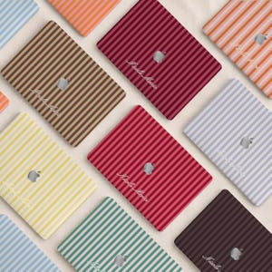 Può includere: Una collezione di skin rettangolari per laptop con vari motivi a righe verticali in colori tra cui marrone, rosso, giallo, verde, arancione e azzurro. Ogni skin mostra un logo Apple argentato centrale e il testo in corsivo Nicole Marie.