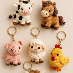 May include: A collection of six crocheted animal keychains featuring a black and white cow, a brown horse, a pink pig, a white sheep, a yellow chicken, and a brown highland cow, each attached to a gold-toned metal split ring and chain.