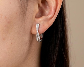 May include: A silver-toned hoop earring featuring a twisted design with one side encrusted with small, clear, sparkling stones. The earring has a polished metallic finish and a secure clasp mechanism, creating a sleek and refined appearance.