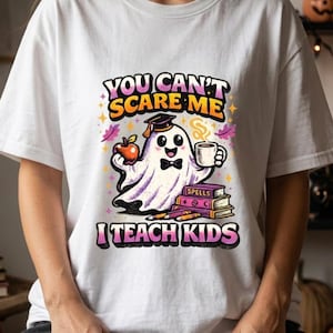 Könnte beinhalten: Ein weißes T-Shirt mit einer Grafik eines Geistes, der eine Doktorhut und eine Fliege trägt und einen roten Apfel sowie eine Kaffeetasse hält. Unter dem Geist befinden sich gestapelte Bücher mit der Aufschrift Spells und Stifte. Text: You Can't Scare Me I Teach Kids.
