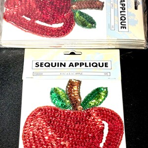 May include: Red sequin apple applique with green and brown accents. The applique measures 4 3/4" x 5 1/2" and is ideal for crafts and embellishments. The package includes the text "SEQUIN APPLIQUE".
