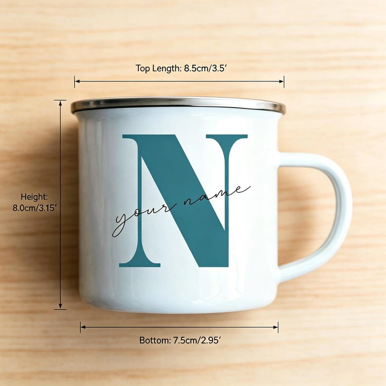 May include: A white enamel mug with a silver rim and a teal letter N printed on the front, accompanied by the text your name. Dimensions are 3.5 inches top length, 3.15 inches height, and 2.95 inches bottom diameter as indicated by labels.