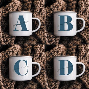 May include: Four white enamel mugs with a silver rim, each featuring a large blue serif letter A, B, C, or D. Below each letter, the text your name is written in a thin, black cursive script. The mugs are arranged in a grid pattern.