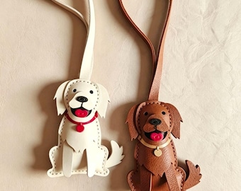 May include: Two dog-shaped leather bag charms with hanging straps. One charm is cream-colored with a red collar and tongue, while the other is brown with a tan collar and red tongue. Both feature stitched details, black noses, and dangling tags.