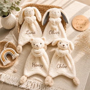 Peut inclure: Quatre doudous en peluche de couleur crème avec les prénoms brodés Luna, Oliver, Henry et Chloe. Deux doudous ont des têtes de lapin, un a une tête d'ours et un a une tête de chiot. Le doudou Oliver présente des oreilles rayées noir et blanc.