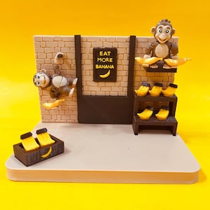 May include: A brown and tan monkey-themed display featuring two monkey figures, one hanging on a brick-patterned wall and one sitting on a shelf. The wall includes a sign that reads EAT MORE BANANA with a yellow banana icon. Yellow bananas are arranged on shelves and in a small brown crate.