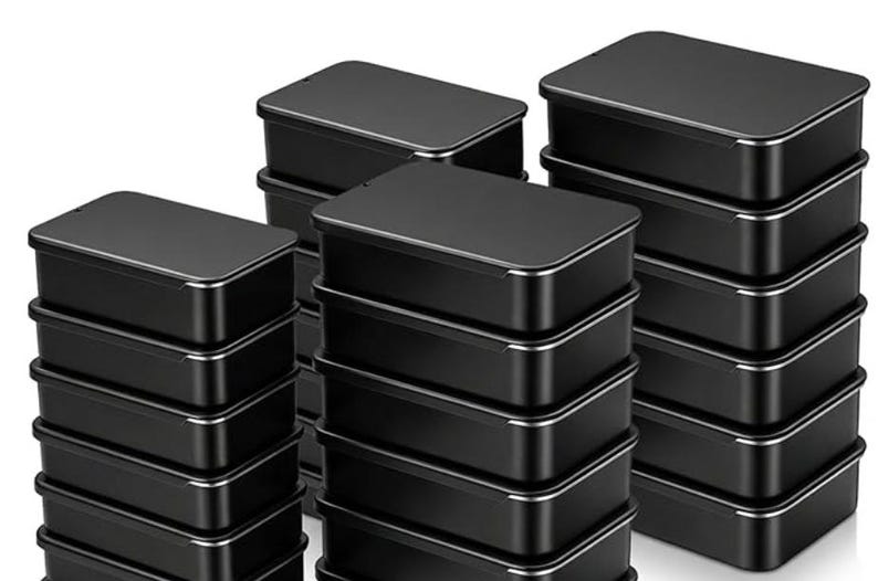 May include: A collection of rectangular black metal tins with lids, arranged in three separate stacks. Each individual container features a smooth matte black finish on the top and sides, with a thin silver-toned metallic rim visible at the base of each lid.