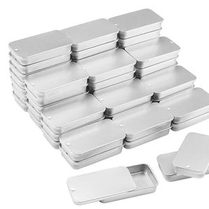 May include: A large collection of rectangular silver-colored metal tins with sliding lids. Each container features a smooth, metallic finish and a small circular indentation on the lid for easy opening. The tins are stacked in multiple rows.