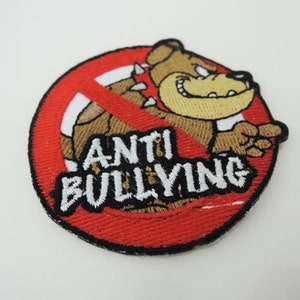 May include: Embroidered patch featuring a cartoon bulldog within a red circle, crossed out with a red line. The patch displays the words "ANTI BULLYING" in white. The bulldog is brown and tan.