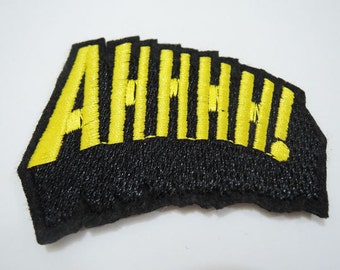 May include: A black fabric patch with yellow embroidered letters that spell out "AHHHH!"