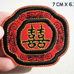 Op de afbeelding: Rode en zwarte geborduurde patch met een gouden Chinees karakter voor "dubbel geluk" in het midden. De patch is 7 cm bij 6,7 cm.