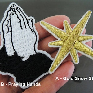Könnte beinhalten: Zwei Bügelbilder, eines mit einem goldenen Sternmuster und das andere mit einem weißen betenden Händen Muster. Das Stern-Patch ist mit "A - Gold Snow Star" und das Patch mit den betenden Händen mit "B - Praying Hands" beschriftet.