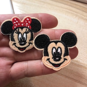 Può includere: Due toppe ricamate da stirare con Mickey Mouse e Minnie Mouse. Mickey Mouse indossa i suoi pantaloncini rossi caratteristici e Minnie Mouse indossa un fiocco rosso a pois.