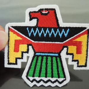 Può includere: Una toppa ricamata colorata che raffigura un uccello nativo americano stilizzato con accenti rossi, gialli, verdi, blu e neri. L'uccello è rivolto in avanti con le ali spiegate.