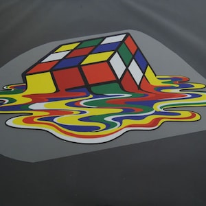 Peut inclure: Un cube de Rubik coloré fondant dans une flaque de couleurs liquides, créant un design surréaliste et abstrait.