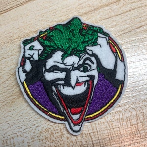 May include: Embroidered patch featuring the Joker from Batman. The Joker is depicted with a green mohawk, a purple background, and a wide, toothy grin.