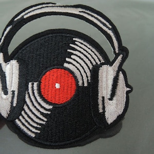 Könnte beinhalten: Ein gestickter Patch in Schwarzweiß, der eine Schallplatte mit roter Mitte in einem Kopfhörer zeigt.