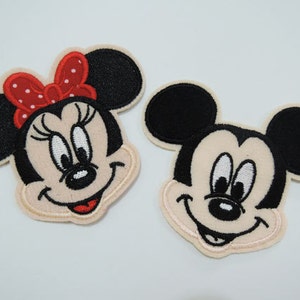Könnte beinhalten: Zwei gestickte Aufnäher mit den Gesichtern von Mickey Mouse und Minnie Mouse. Mickey Mouse trägt seine charakteristischen roten Shorts und Minnie Mouse trägt eine rote Schleife mit weißen Punkten.