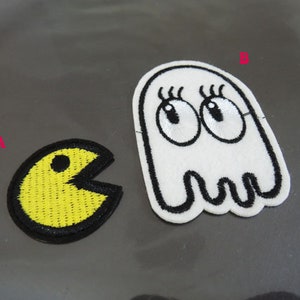 Può includere: Due toppe ricamate da stirare, una con il personaggio giallo di Pac-Man e l'altra con un fantasma bianco con occhi e ciglia neri.