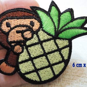 Könnte beinhalten: Gestickter Aufnäher mit einem braunen Affen, der eine grüne Ananas mit braunem Stiel und grünen Blättern hält. Der Aufnäher misst 6 cm x 7 cm.