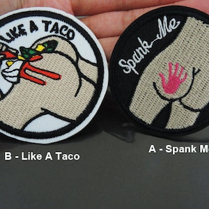 May include: Two embroidered patches. One is black with white text that says "Spank Me" and a pink handprint. The other is white with black text that says "Like A Taco" and a cartoon image of a person eating a taco.