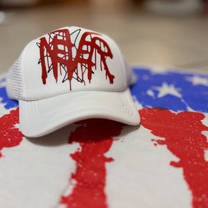 Puede incluir: Una gorra tipo trucker blanca con panel frontal estructurado y parte trasera de malla. El frente presenta un diseño gráfico rojo audaz de estilo goteo con el texto "NEVER" superpuesto sobre el contorno de una estrella negra.
