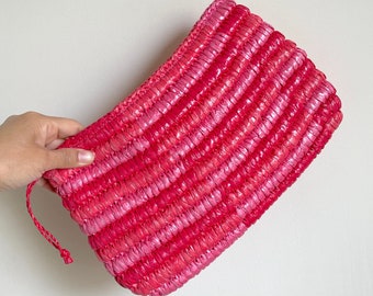 May include: A pink and red woven clutch bag with a drawstring closure.