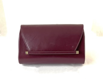 May include: A burgundy leather clutch purse with a gold metal bar closure.