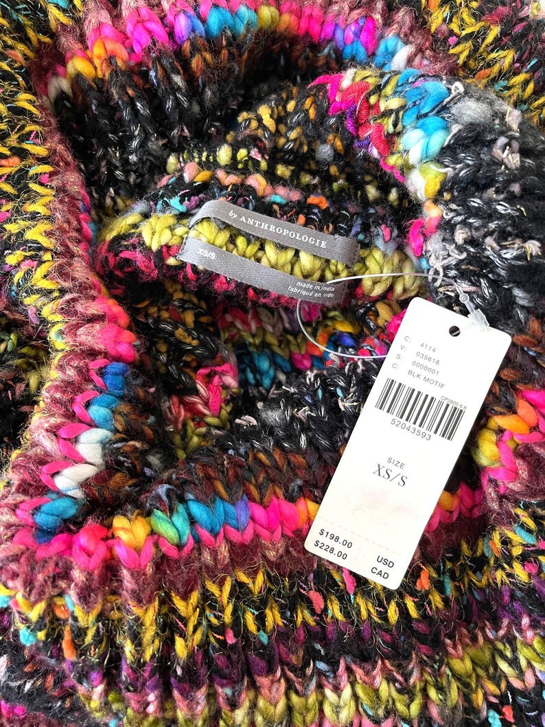 Op de afbeelding: Een veelkleurige gebreide trui met een zwarte achtergrond. De trui heeft een hoge hals en is gemaakt van een dik garen. Het label zegt "By Anthropologie" en "XS/S".