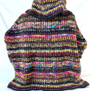 Op de afbeelding: Een kleurrijke gestreepte trui met een hoge hals en een zwarte basis en een verscheidenheid aan felle kleuren, waaronder roze, geel, groen en blauw.