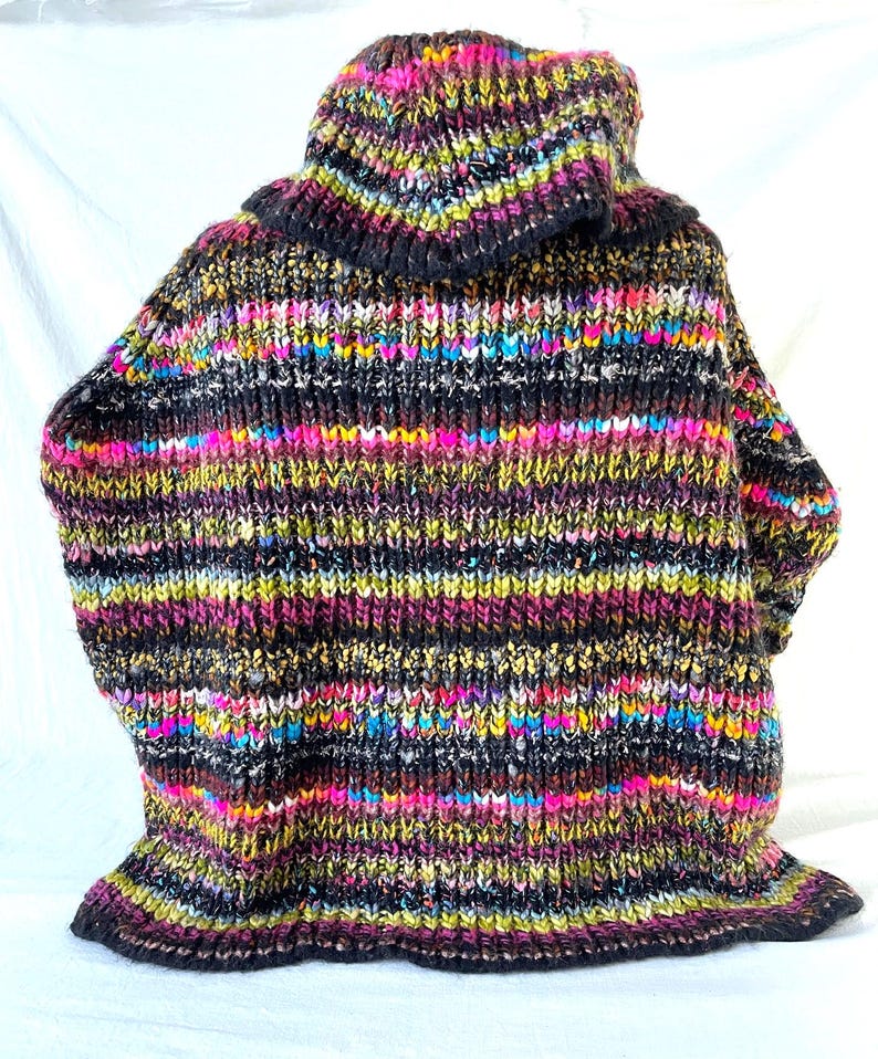 Op de afbeelding: Een kleurrijke gestreepte trui met een hoge hals en een zwarte basis en een verscheidenheid aan felle kleuren, waaronder roze, geel, groen en blauw.