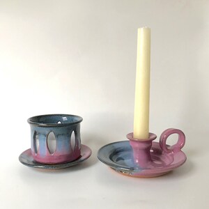 May include: Two handmade ceramic candle holders. One is a small cup with oval cutouts, and the other is a candle holder with a handle. Both are painted with a gradient of blue, pink, and purple.