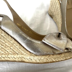 May include: Metallic silver wedge sandals with a bow detail. The sandals have a woven jute sole and a slingback strap. The shoes are marked "Made in Italy 36".