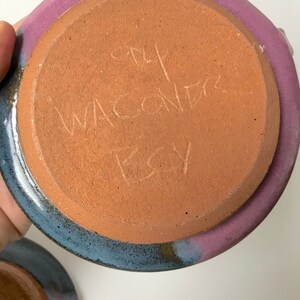 May include: Handmade ceramic pottery with a purple and blue rim and a terracotta base. The base has etched text that reads "The Wacondr Etsy". The pottery is a unique piece of art.
