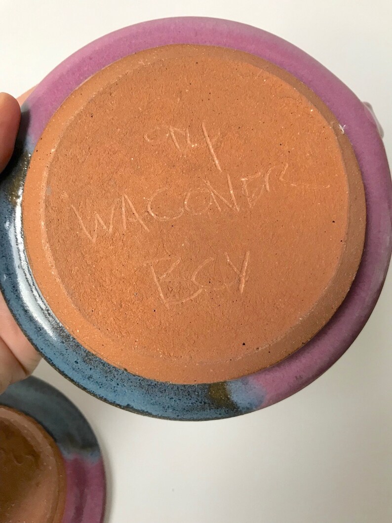 May include: Handmade ceramic pottery with a purple and blue rim and a terracotta base. The base has etched text that reads "The Wacondr Etsy". The pottery is a unique piece of art.