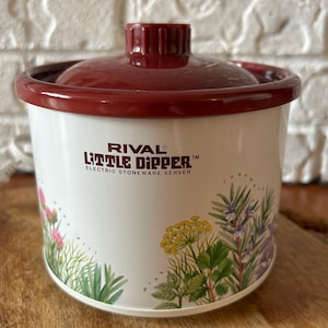 May include: A white Rival Little Dipper electric stoneware server with a dark red lid. The exterior features a botanical print of green herbs and yellow flowers. The text on the front reads Rival Little Dipper Electric Stoneware Server.