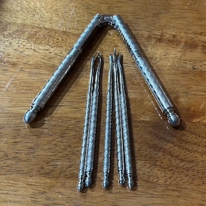 May include: A silver-toned metal nutcracker with a textured, cross-hatched pattern on the handles and a hinged joint, accompanied by four matching slender metal picks with pointed, slightly curved ends and a similar textured finish on the handles.